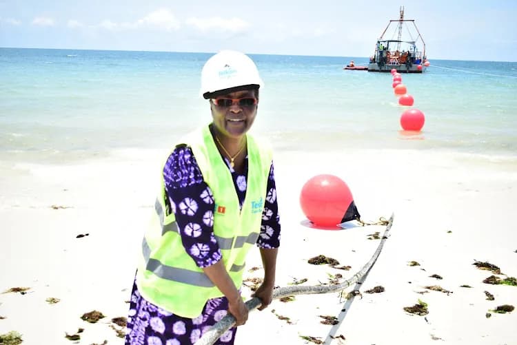 Landing crew guiding a submarine cable ashore on a Kenyan beach, with marker buoys running out to the cable ship offshore